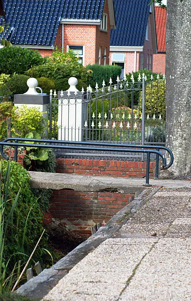 picture taken in the Netherlands, Leek provence Groningen in the North. Typical Dutch houes in the region have a small ditch in front of the houses. Every houe has it's own, typical bridge over that ditch in front of house. Here's the contrast of a very old one, where the neighbours have a brandnew fence.