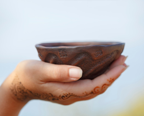 Female hand with traditional Indian wedding henna mehendi pattern holds a clay cup with widespread ethnic symbols.