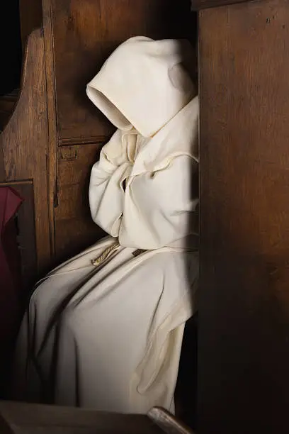 Monk with hood sitting in a wooden corner of a medieval church