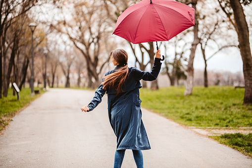 Beautiful young woman holding a red umbrella in the public park in autumn.