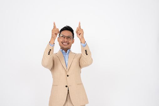 A handsome Asian businessman is pointing his finger up an empty space on an isolated white background. showing options, recommendation, advice, presentation