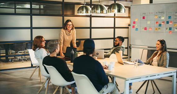 Business people in a boardroom are engaged in a lively discussion. They work together as a team, brainstorming creative ideas for a successful tech company project. Guided by a confident leader, their collaboration fosters a professional and innovative workplace environment.