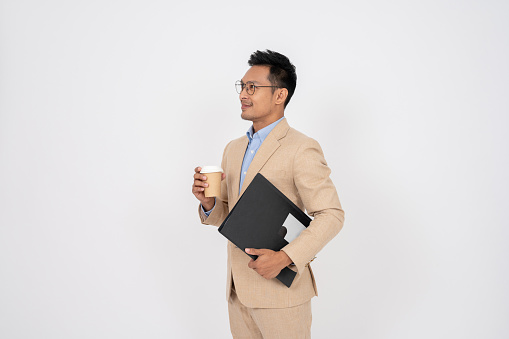 A successful and experienced Asian businessman in a formal suit with a document binder is looking aside at an empty space on an isolated white background.