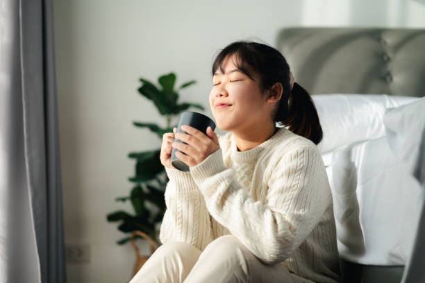 istock Young woman drinking coffee in bedroom, Holding coffee cup with two hands 1866748464