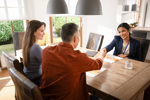 Couple handshakes with financial advisor while sitting at dining table in house.