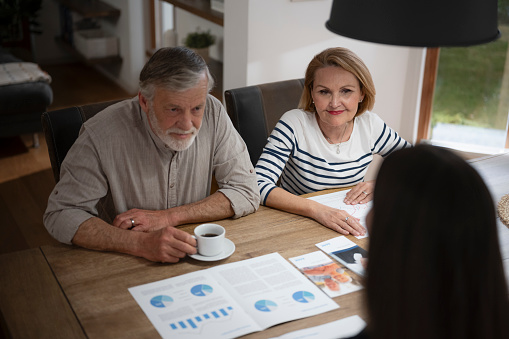 Senior couple discussion with financial advisor while sitting at dining table in house.