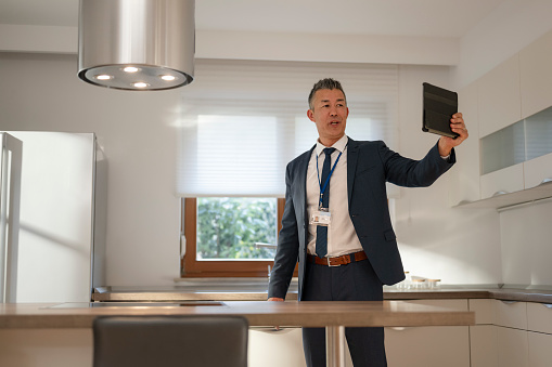 Male real estate agent showing kitchen in luxury house during video conference call on digital tablet.