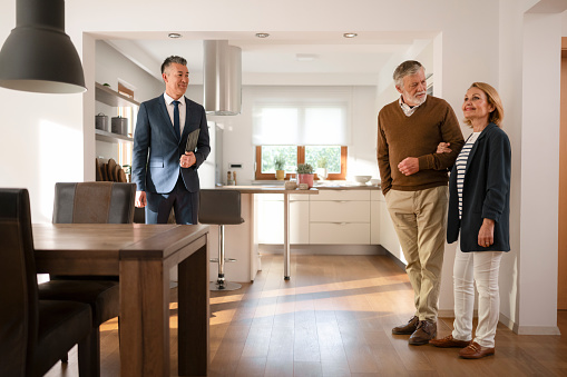 Male real estate agent showing modern luxury house to senior couple while standing in kitchen.