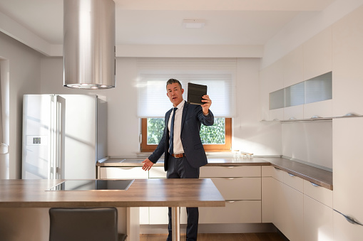 Male real estate agent showing kitchen in luxury house during video conference call on digital tablet.