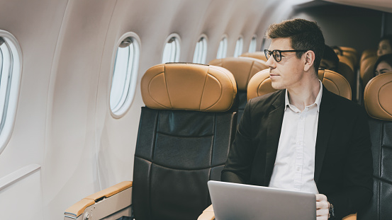 Businessman traveling by plane look at the window. Caucasian male passenger sitting in the flight airline cabin business class travel business contacts.