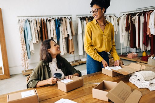 Successful business women smiling at each other as they fulfil orders made on their online clothing store. Happy female entrepreneurs running a dropshipping business as a team.