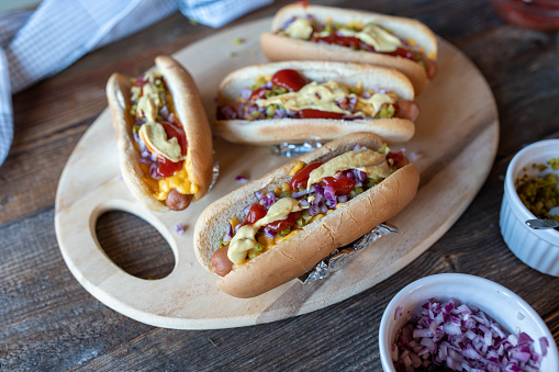 Delicious fast food or party food for new years eve, birthday partys or as a easy familie meal with fresh oven baked hot dogs. Baked with cheese and topped with red onions, mustard, pickles and ketchup. Served ready to eat on a table.