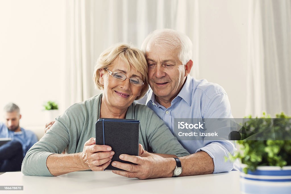 Senior couple with e-reader Cheerful senior couple sitting by the table at home and reading an e-book. Couple - Relationship Stock Photo