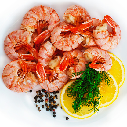 Set of unpeeled shrimps with lemon, green dill and spices on a white background. View from above.