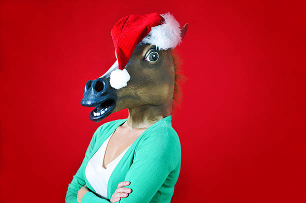 A young woman with a horse mask wears a Santa hat. She is ready to party. Horizontal image with copy space.