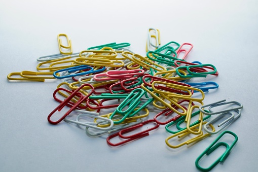 Multicolored paper clips on a white background in a scattered form