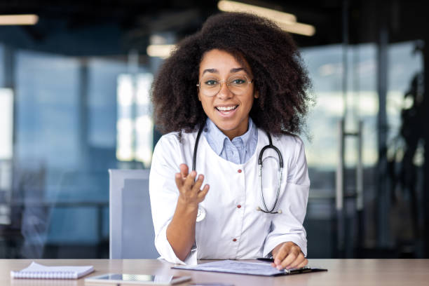 istock Web camera view, screen, female doctor talking remotely with patients, consulting, happy looking at camera, gesturing with hands, female doctor in white medical coat inside clinic office 1866797321