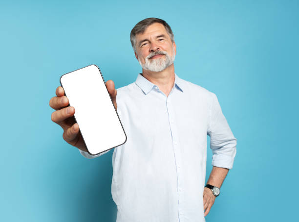 istock Handsome Excited Mature Man Showing Pointing At Empty Smartphone Screen Posing Over Light Blue Studio Background, Smiling To Camera. Check This Out, Cellphone Display Mock Up 1866802590