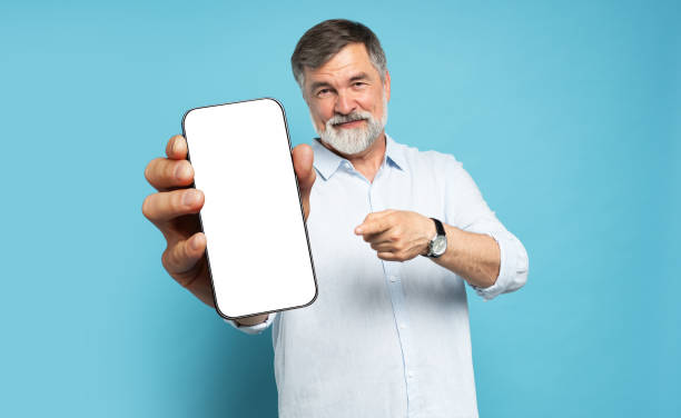 istock Handsome Excited Mature Man Showing Pointing At Empty Smartphone Screen Posing Over Light Blue Studio Background, Smiling To Camera. Check This Out, Cellphone Display Mock Up 1866802600