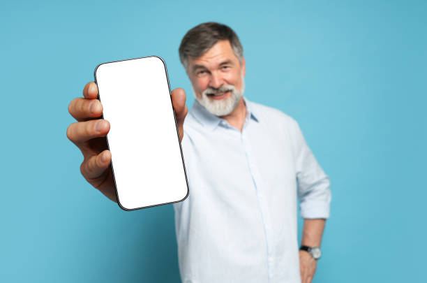 istock Handsome Excited Mature Man Showing Pointing At Empty Smartphone Screen Posing Over Light Blue Studio Background, Smiling To Camera. Check This Out, Cellphone Display Mock Up 1866802603