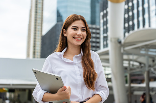 Portrait of Asian youg beautiful businesswoman standing outdoor in city. Attractive employee girl worker feel happy and confident then smile, looking at camera. Job application and recruitment concept