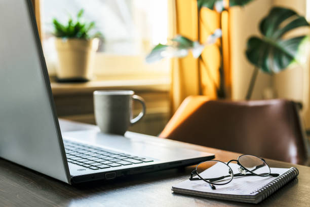 istock Laptop, notebook and glasses on table in room with home plants 1866825232