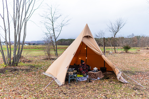 A view inside an open tepee style winter tent with one woman sitting inside.