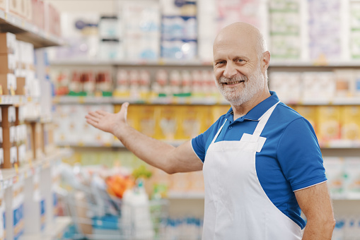 Portrait of a smiling grocery clerk at the supermarket, he is welcoming customers at the store