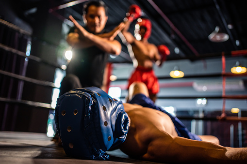 Caucasian professional sport young man loser exercise in fitness club. Attractive athlete in sportswear and boxing gloves fainting and falling on the ground after competitor punching in gym stadium.