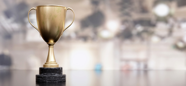 Gold steel trophy cup with dual handle on empty blur background. A reminder of a specific achievement, shiny metallic reward. Copy space. 3d render