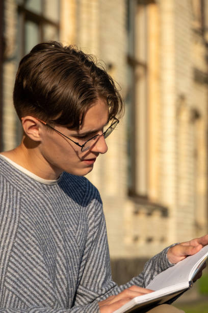 istock Guy with glasses prepares for exams by reading textbook 1866866019