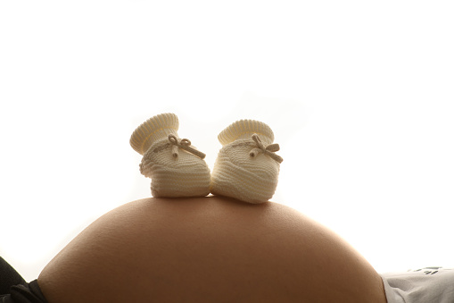 2 small baby booties on a belly of a pregnant woman on a white background
