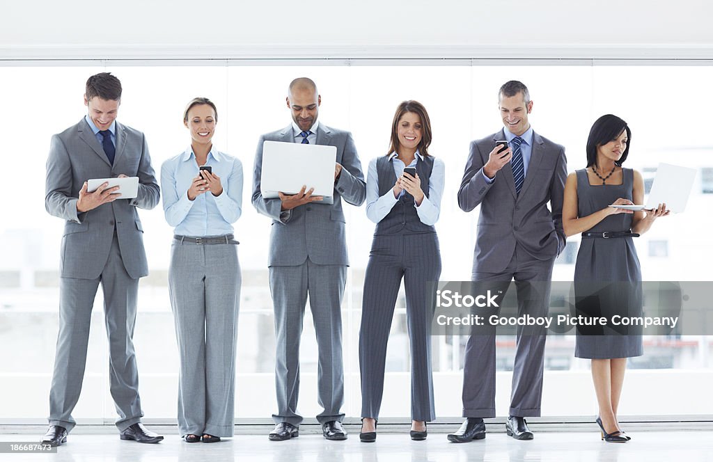 Communication technology A multi-ethnic group of businesspeople standing in a row holding various electronic communication devices 30-39 Years Stock Photo
