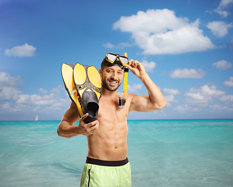Man in swimwear with a mask and snorkeling fins in front of a sea on Cuba