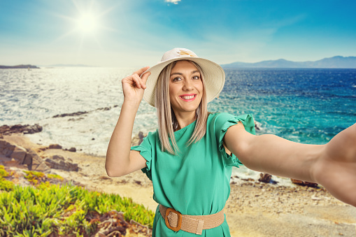 Happy young woman with a straw hat taking a selfie at a beautiful place near the sea