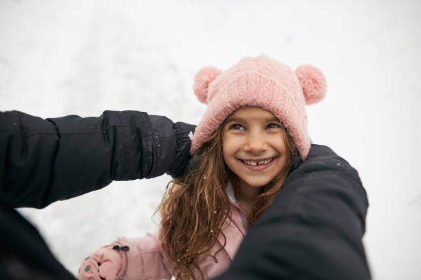 Father and daughter having fun on winter day. He is putting hat on her head.