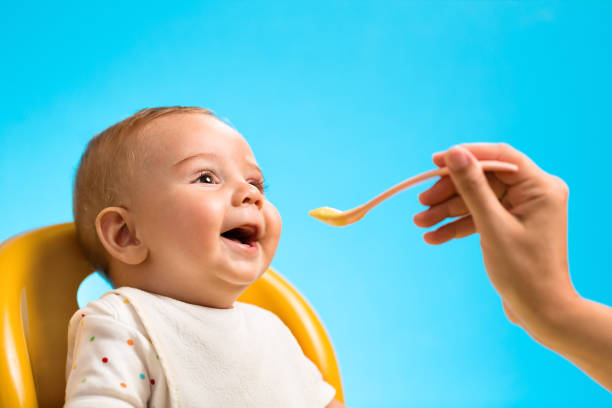 Feeding baby Mother's hand feeding a laughing baby in front of a vivid blue background. baby spoon stock pictures, royalty-free photos & images