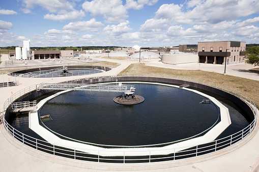 A municipal waste water treatment plant circular center feed clarifier tank with skimmer. This tank removes heavy solids by settling and separation from the water. The skimmer removes scum from the water surface. Below the water surface scraper blades remove sludge from the bottom of the tank. The saw teeth (weir) allows clarified water to slowly exit the tank while retaining solids. Other plant operations are visible in the background.