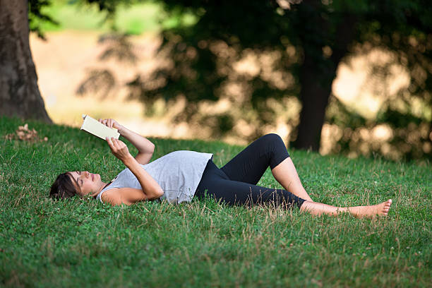 istock Pregnant woman reading a book lying on the grass 186690896