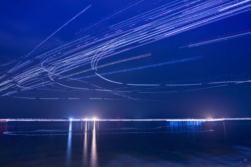 Light trails of airplanes taken off from airport nearby during the night, sea as foreground.
