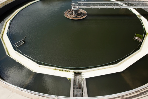 A municipal waste water treatment plant circular center feed clarifier tank with skimmer and bridge. This tank removes heavy solids by settling and separation from the water. The skimmer removes scum from the water surface. Below the water surface scraper blades remove sludge from the bottom of the tank. The saw teeth (weir) allows clarified water to slowly exit the tank while retaining solids.