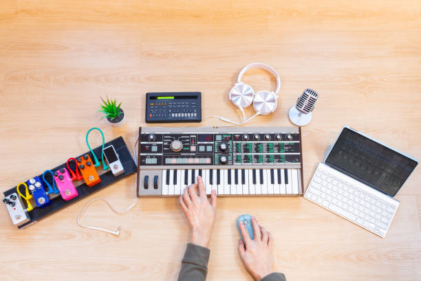 istock male musician hands playing keyboard synthesizer with tablet computer, sequencer, effect processor, headphone and microphone on wooden desk. music production concept 1866948833