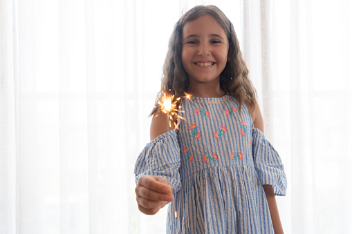 Little girl smiling out of focus background with sparkler in hand in foreground