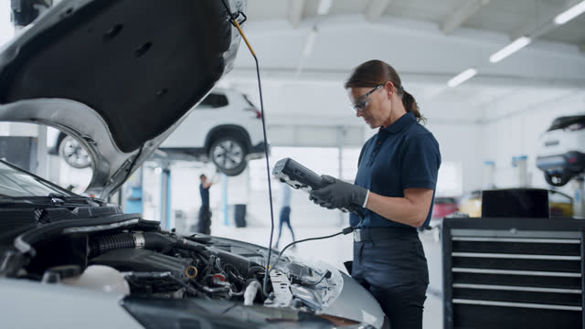 Female mechanic running diagnostics test on car engine in repair shop