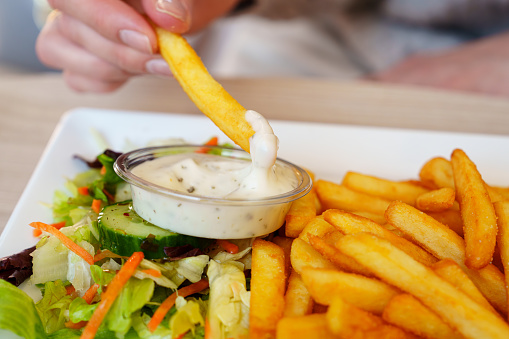 Woman hand dipping delicious French fries into mayonnaise sauce, cheese sauce. Hand hold a french fries and dips it in sauce tartar