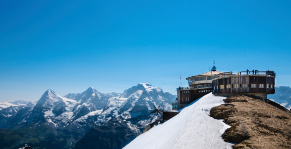 The observation deck and restaurant at the top of the Schilthorn in the Bernese Alps, Switzerland. Tourists can be seen on the observation deck. The Jungfrau, Monch and Eiger mountains can be seen in the background.