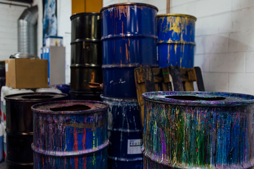 A close-up shot of metal drums filled with different coloured ink in an ink factory in Hexham, North East England. They are in an industrial warehouse and there is lots of ink covering the outside of the drums where it has spilled out of the containers.