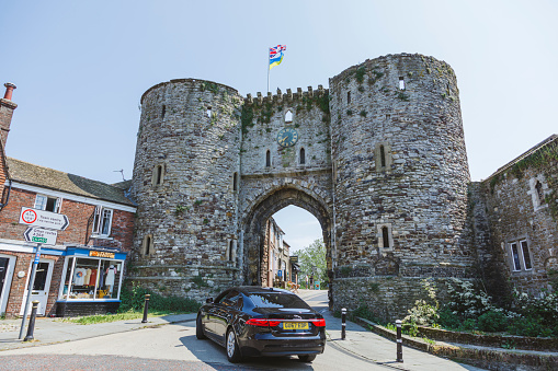 Rye, United Kingdom - Jun 13, 2023: The Landgate in Rye, East Sussex, England, a 14th century fortified gateway in the town walls standing on East Cliff. At one time there were four gates with Landgate being the only one to open on to dry land. An antique shop takes advantage of the fine weather to display its wares on the cobbled pavement.