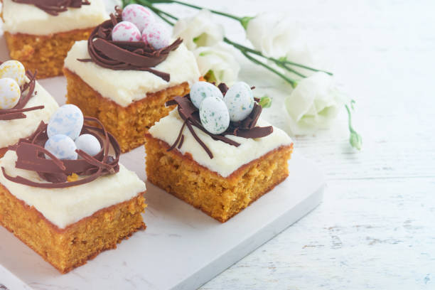 istock Easter carrot cake bars decorated with chocolate nest and chocolate candy eggs blossoming cherry or apple flowers on rustic light wooden backgrounds. Easter holiday meal. Traditional Easter food. 1867030349