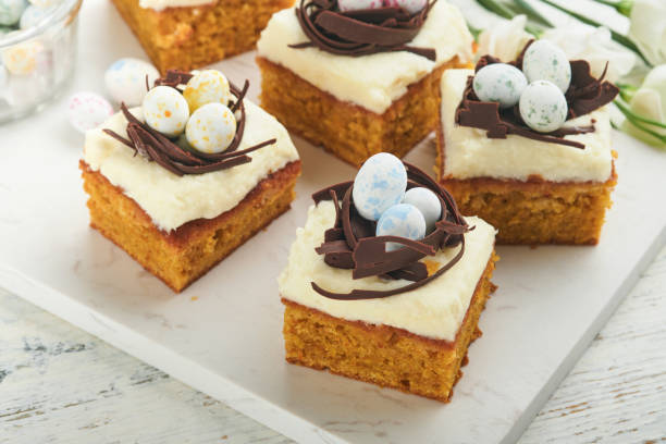 istock Easter carrot cake bars decorated with chocolate nest and chocolate candy eggs blossoming cherry or apple flowers on rustic light wooden backgrounds. Easter holiday meal. Traditional Easter food. 1867031446